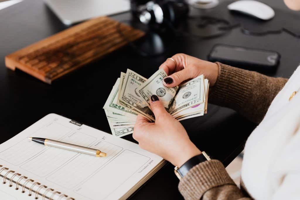 Person counting twenty-dollar bills at a desk with a planner