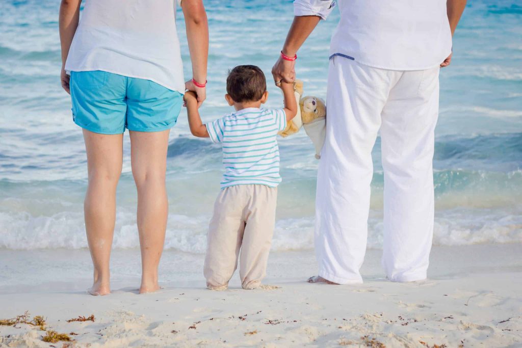 Young child holding both parents' hands on a beach