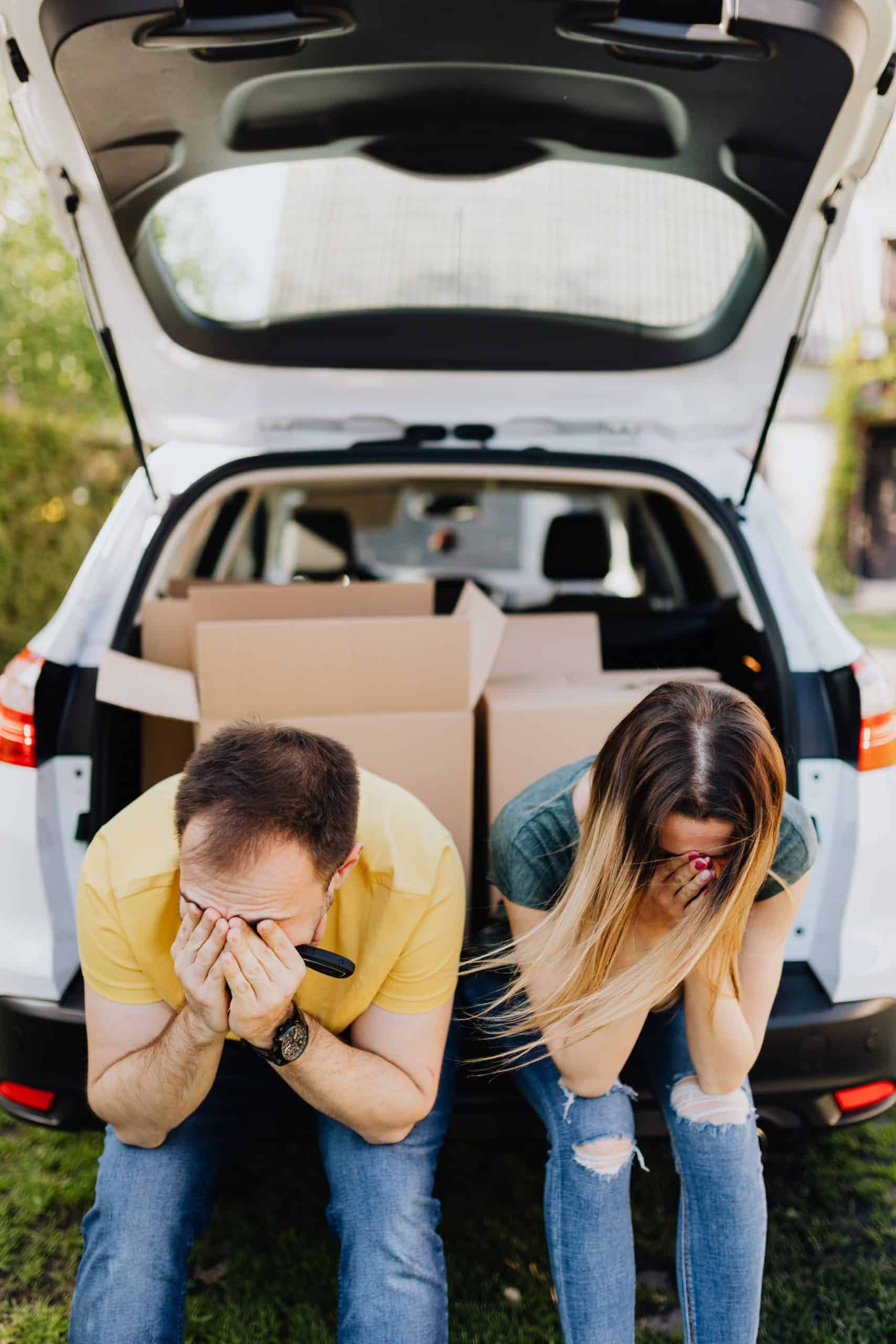 Distressed couple sitting at the open trunk of a car filled with moving boxes