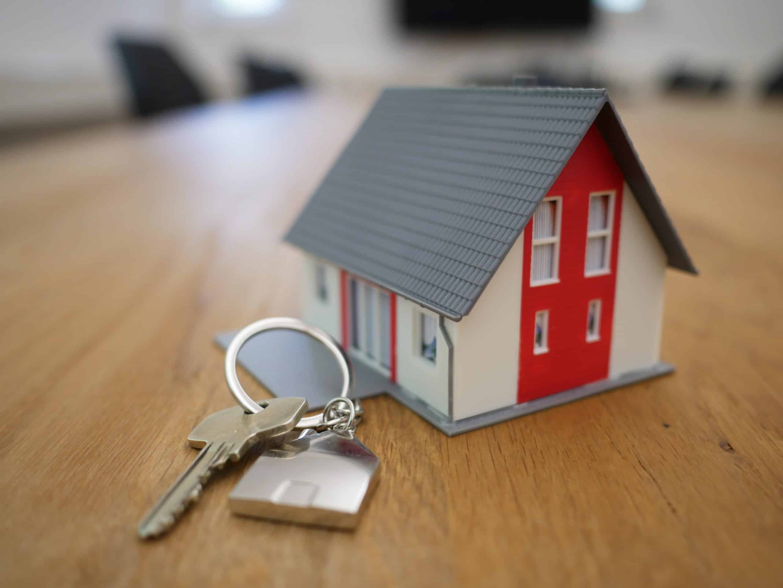 House key with a house-shaped keychain beside a model home